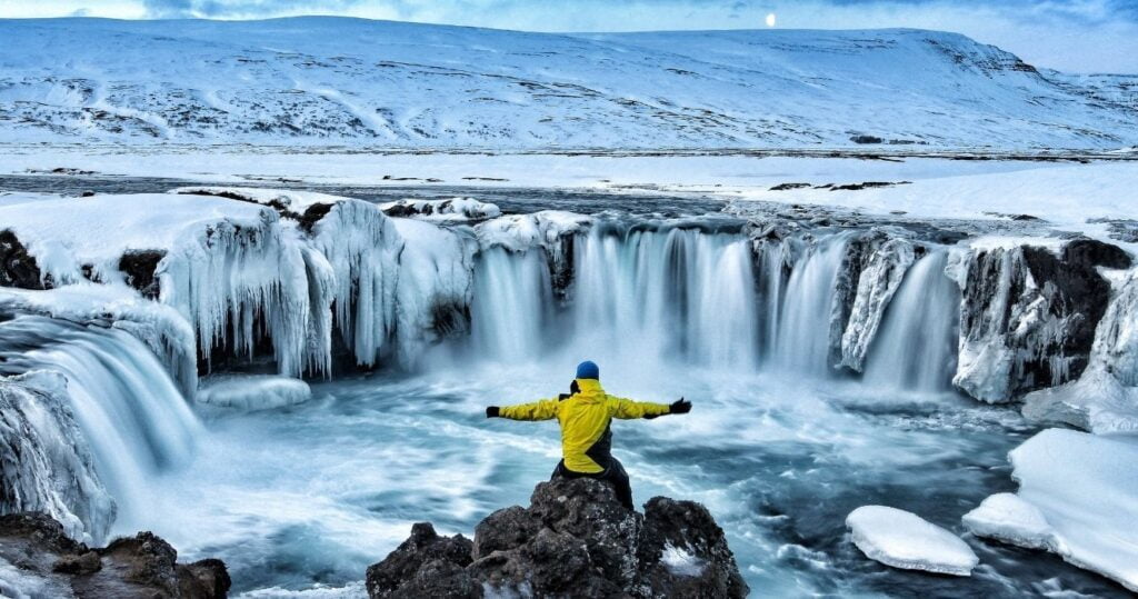 a hiker sitting at the edge of a frozen waterfall in iceland in the winter
