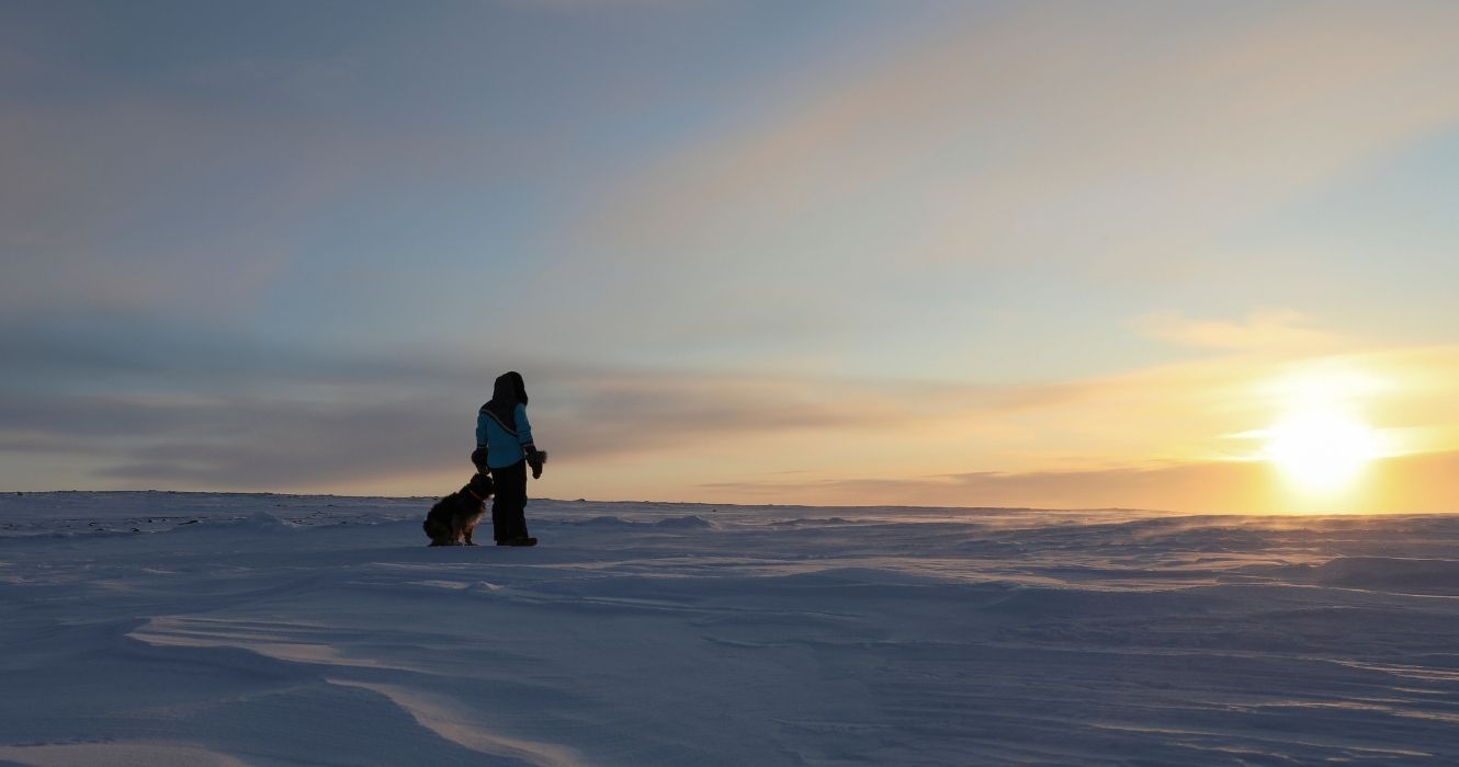uma pessoa em pé com seu cachorro no ártico nunavut